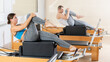 © JackF - Positive young girl performing set of pilates exercises on reformer with box during group workout in fitness studio. Healthy active lifestyle..