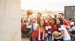 © SimpleDesignStudio - Diverse Group of Young Adult Friends Cheering for Soccer Match on Rooftop Terrace with Fans Scarves and Balls