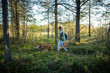 © DimaBerlin - Woman forager accompanied by Vizsla dog walking through autumn pine forest collecting mushrooms, female hiker with pet searching for edible boletus mushrooms, traditional fall season leisure activity.