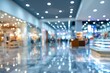 © morepiixel - Blurred image of a modern shopping mall interior with bright ceiling lights, polished floors, and various store displays creating a lively, commercial atmosphere.
