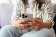 © simona - A relaxed woman sitting on a couch holding a smartphone in both hands, scrolling and texting while wearing a striped shirt and jeans, focused on social media, communication and digital lifestyle.