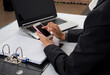 © apimook - Businesswoman using smartphone at office desk with laptop and document folder.