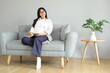 © ArvStd - A young woman relaxes sitting on the sofa at home, occasionally looking up, remembering something and writing in a notebook, spending her free time in the living room.