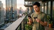 © Таня Андреева - Asian man using smartphone and credit card on city apartment balcony.