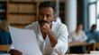 © Martin - Salvadoran IT professional reviewing his H1B denial notice at a public library table, law library books behind him, other patrons blurred in background, visa rejection stress, employment immigration