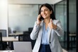 © Asier - Businesswoman giving thumbs up gesture during a successful phone call in a modern office workplace