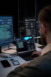 © DragonImages - Vertical shot of young adult man monitoring cybersecurity dashboards across laptop and desktop screens, analyzing network data and threat alerts. Ideal for IT security, data protection, cyber defense