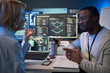 © DragonImages - African American young adult man discussing cybersecurity data with middle aged Caucasian woman at workstation. Supporting IT consulting, software development, team strategy