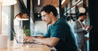 © peopleimages.com - Man, typing and remote work in restaurant with laptop, research or check trends for graphic design. Freelancer, person or creative designer in cafe with computer, editing project or digital campaign.