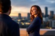 © Leo Rohmann - Confident businesswoman standing on a rooftop at sunset with city skyline and colleague in the foreground