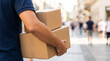 © Olga Ко - Primer plano de un repartidor irreconocible llevando cajas de cartón por una calle peatonal de la ciudad. Concepto de servicio de entrega, logística y compras online.