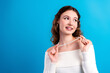 © deagreez - Young woman smiling and holding a pearl necklace in a stylish off-shoulder sweater on bright blue background