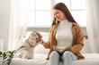 © Pixel-Shot - Young woman with cute Scottish Fold cat reading book in bedroom