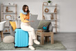 © Pixel-Shot - Female traveler with laptop sitting on suitcase at home. Itinerary concept
