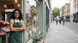 © Vera D - Smiling young Indian woman florist wearing green apron standing with crossed arms at the entrance of her flower shop on a city street. Small business owner portrait.
