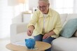 © New Africa - Pension fund. Senior woman putting money into piggybank at table indoors. Space for text