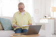 © New Africa - Pension. Senior woman with paperwork, money and laptop at table indoors. Space for text