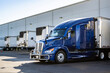 © vit - Dark blue big rig semi truck with grille guard loading cargo into refrigerated semi trailer standing in the warehouse dock gate