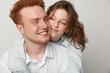 © SHOTPRIME STUDIO - Happy young couple with red hair embraces and smiles in casual white clothing. Close affectionate moment with natural expressions on neutral background. Concept of love and friendship.