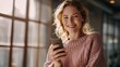 © Pichkan - Smiling Woman Holding Smartphone Confidently in Warm Cozy Indoor Setting