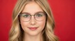 © Aku - Portrait of a smiling young blonde girl wearing stylish eyeglasses against a red background.