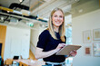 © we.bond.creations - Young business woman smiling, using a digital tablet for work in a modern office environment. Professional female employee at work