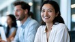 © Thares2020 - A smiling professional woman is featured in a bright modern office setting with a colleague in the background emphasizing teamwork and collabo n