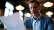 © Thares2020 - A focused professional man in a blue shirt reviews a document in a bright modern office setting