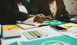 © Sutthicha - Corporate team discussing ESG goals and clean energy strategies in conference room, reviewing sustainable supply chain documents and laptop presentation, business sustainability