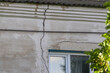 © Marina - Large deep vertical crack on the old concrete stucco facade of a residential house wall running down from the roof line, building structural failure and property insurance concept.