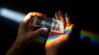© Ai Guy - A hands holding a prism dispersing light into a vibrant rainbow spectrum across dark background
