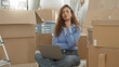 © Krakenimages.com - Woman with laptop, finger to cheek while seated among moving boxes in building; contemplative planning.