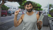 © Krakenimages.com - Man in gray tank top holding a shampoo bottle and pointing right index finger up on a busy street with trees and parked cars; casual confidence.