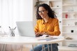 © Prostock-studio - Smiling Latin American Woman Sitting At Table Working On Laptop In Modern Home Office, Enjoying Productive Day, Focusing On Task With Happy Expression. Business Concept.