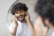 © Prostock-studio - Happy Young Man With Curly Hair Applying Yellow Eye Mask In Front Of Mirror At Home, Enjoying Skincare Routine In Modern Bathroom. Focused On Personal Care And Wellness Concept.