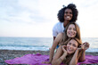 © SISMIZ - Three diverse women enjoying a sunny day at the beach, stacked playfully on a blanket