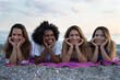 © SISMIZ - Four diverse women smiling and resting on a beach towel by the sea
