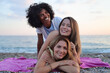 © SISMIZ - Three diverse women smiling and embracing on a beach towel at sunset
