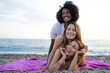 © SISMIZ - Three diverse women laughing and enjoying a beach day together on a purple towel