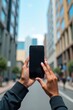 © Leonardo - Imagen editorial, manos sosteniendo un teléfono al aire libre en una calle de la ciudad, edificios