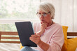 © Tatyana Gladskih - Senior woman sitting on couch and looking at tablet screen. Focused elderly lady using digital device at home. Modern technology for retired person for communication and entertainment.