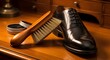 © Waqf - Shoe brush and polish kit rest beside a formal leather dress shoe on a polished wooden desk surface.