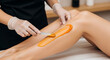 © tu - Professional beautician performing hair removal treatment by waxing a female leg in a modern wellness spa or beauty salon using a hot wax strip for smooth skin and body care hygiene.