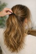 © Fotograf - A woman in a white sweater is combing her hair, focusing on her grooming