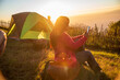 © aFotostock - Women camping outdoor sitting Tent Camp trip hiking mountain hill on sunrise. Picnic green nature campground Adventure Travel wildness forest. Tent camp in nature background flare sunlight mountain