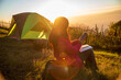 © aFotostock - Women camping outdoor sitting Tent Camp trip hiking mountain hill on sunrise. Picnic green nature campground Adventure Travel wildness forest. Tent camp in nature background flare sunlight mountain