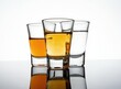 © miss irine - Three shot glasses filled with different alcoholic beverages stand on a reflective surface. Two glasses contain amber liquids, one clear. The backdrop is pure white.