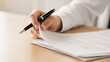 © Jahanzaib - Close-up of a person holding a luxury pen while flipping through pages of a business contract document on a wooden desk