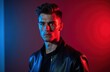 © Vadym - Young man with stylish hair wears leather jacket. Dual colored lighting casts red and blue shadows on his face. He looks seriously forward, exuding confidence and modern appeal.