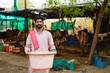 © Niks Ads - A young indian farmer standing confidently in a rural cattle farm holding a large plastic tub